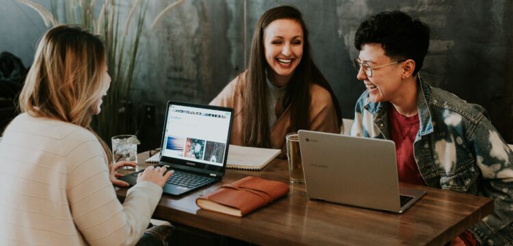 decorative image: a group of three students having fun while working on their laptops
